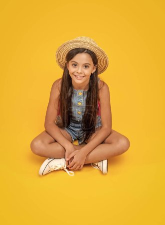 Téléchargez les photos : Heureux adolescent fille en paille chapeau assis sur fond jaune. - en image libre de droit