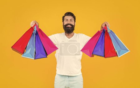 Téléchargez les photos : Photo d'un commerçant souriant avec des sacs. shopping homme isolé sur jaune. magasinier en studio. shopping homme sur fond. - en image libre de droit