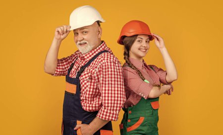 positive kid and grandfather builder in helmet on yellow background.