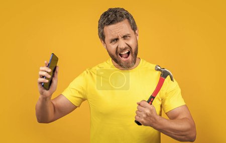Mann schockt und hackt das Telefon isoliert auf gelb. Mann hackt das Telefon im Hintergrund. Mann hackt Telefon im Studio. Foto eines Mannes, der das Telefon mit einem Hammer hackt.