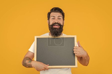 happy man offer advertisement in studio. photo of man offer advertisement at blackboard. bearded man offer advertisement isolated on yellow. man offer advertisement on background with copy space.