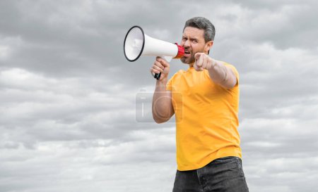 man in yellow shirt shout in megaphone on sky background. pointing finger.