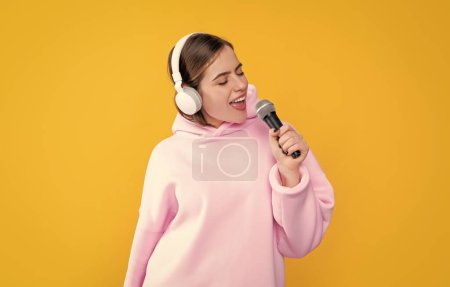 Téléchargez les photos : Positive jeune fille dans les écouteurs avec microphone sur fond jaune. - en image libre de droit