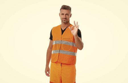 mature man worker show ok gesture isolated on white. worker man in orange uniform. worker man wearing working reflective vest. studio shot of man worker.