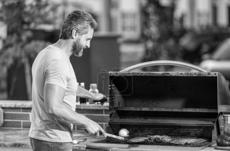 man with hot grill at a barbecue party. Talented barbecue enthusiast. man grilling delicious barbecue on a summer day. man preparing grilled food at backyard barbecue. rib eye steak.