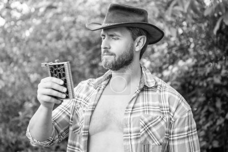 Photo for Masculine cowboy with whisky flask. masculine cowboy with flask. masculine cowboy with flask outdoor. masculine cowboy with flask wear hat. - Royalty Free Image