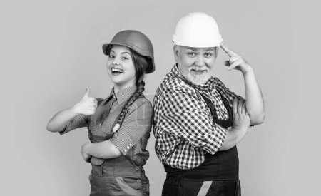 happy girl and grandfather builder in helmet on yellow background. thumb up. builder concept. fathers day