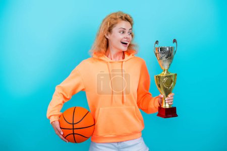 Erfolg feiern. Das Spiel gewinnen. Sportleistungsabzeichen. Frau mit Basketballball und Meisterschale. Glückliche Basketballspielerin. Sportlicher Erfolg. Die Frau gewann den Preis. Spitzenathlet.