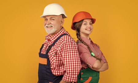 smiling teen child and grandfather builder in helmet on yellow background.