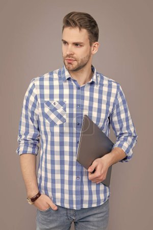 Serious man holding laptop computer. Freelancer with laptop device. Laptop user studio isolated on grey.