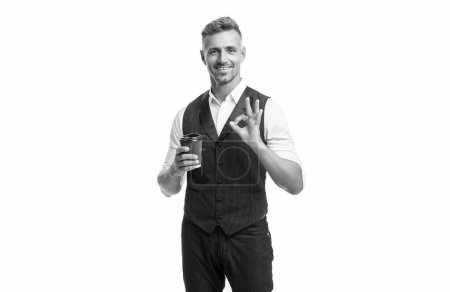 Happy manager in suit vest showing OK ring gesture holding disposable cup with takeaway tea isolated on white.