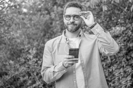 Photo for Smiling man messaging on phone, copy space. man messaging on phone outdoor. man messaging on phone or checking email. photo of man messaging on phone. - Royalty Free Image