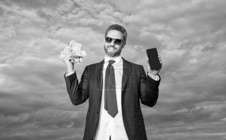 Happy rich man businessman holding cash money and smartphone. Money transfer. Cash payment or smartphone payment. Cash purchase. Paying in cash.