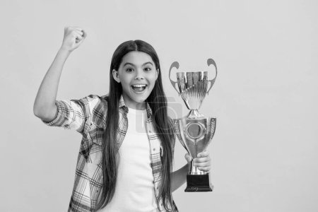 successful proud teen girl with champion cup award isolated on yellow.