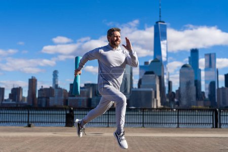 Sportsman running with fitness mat. Sport man training outdoor in New York. Healthy lifestyle with daily fitness. Fitness and sport. Man running with energy. Sport lifestyle. Set a running goal.