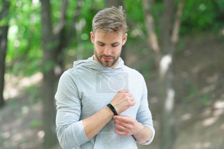 Sporty fit man with sport equipment checks time on smartwatch. Man tracking fitness results dressed in sportswear outdoor. Man runner with fitness gadget. Smartwatch for fitness.