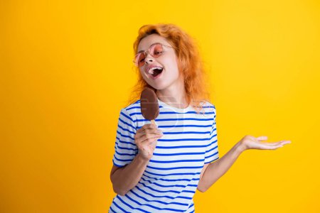 Woman with a cornet ice cream. Delicious waffle cone in summer. Girl eating ice cream in summer. Happy young woman with delicious ice cream in cone isolated on yellow. Presenting product.