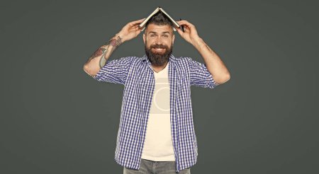 happy bearded man with book on head on grey background.