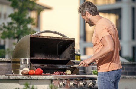 Mann grillt Steaks in Perfektion auf verrauchtem Grill. Barbecue-Kochkunst. Grillmann kochen Fleisch am Grill. Mann im Freien kocht Grill und Grillgerichte.