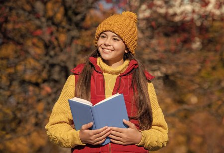 niño adolescente feliz leer el libro escolar en otoño.