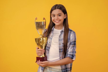 positive proud teen girl with champion cup award. teen girl hold her award champion cup isolated on yellow. teen girl receive award in studio. teen girl accept award on background.