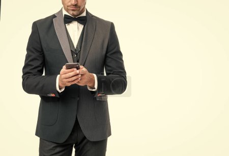 mature tuxedo man messaging on smartphone isolated on white background.