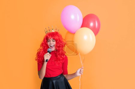 cheerful child in crown with microphone and party balloon on yellow background.