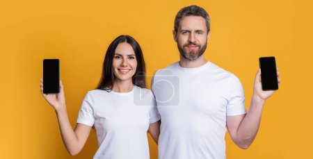 Couple showing smartphone isolated on yellow. Man and woman showing phone app. Family blog. Product proposal. Advertisement presentation copy space. Couple presenting phone screen. Video calls.