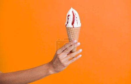 Gelato ice cream cone. Ice cream cone isolated on orange. Summer vanilla taste. Woman holding the ice cream by hand. Ice cream in hand. Yummy summer gelato. Authentic Italian gelato.