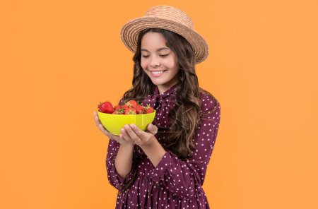 happy teen kid hold strawberry bowl on yellow background.