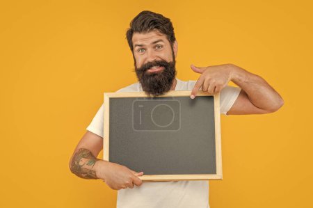 image of man presenting sale at blackboard. bearded man presenting sale isolated on yellow. man presenting sale on background with copy space. man presenting sale in studio.