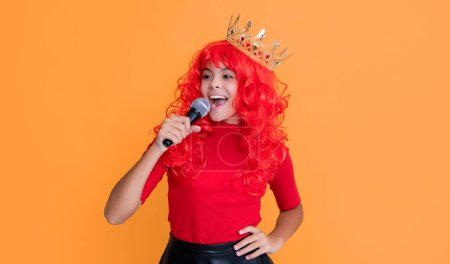 smiling kid in crown with microphone on yellow background.
