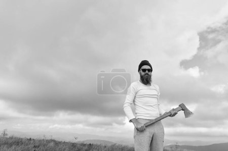 brutal bearded man lumberjack hold axe outdoor. bearded man lumberjack has axe. bearded man lumberjack with axe. photo of bearded man lumberjack holding axe in the mountain.