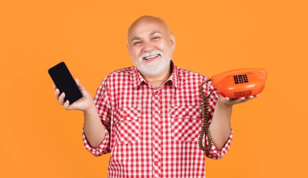 Téléchargez les photos : Happy smiling old man with retro telephone and modern smartphone on yellow background. - en image libre de droit
