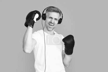 successful man boxer in sport boxing gloves wear headphones. photo of man boxer in sport boxing gloves. man boxer in sport boxing gloves isolated on blue. man boxer in sport boxing gloves at studio.