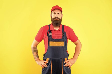 serious bearded man repairer in work clothes on yellow background.