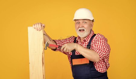 surprised senior man woodworker in helmet on yellow background.