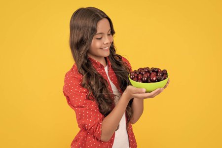 smiling teen girl hold cherry bowl on yellow background.