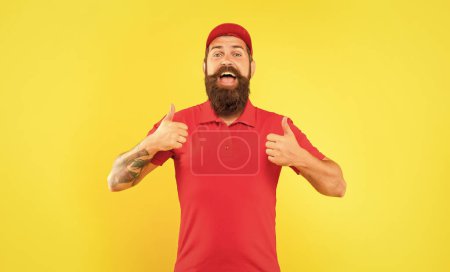 Happy bearded man in casual red cap and tshirt giving double thumbs yellow background, deliveryman.