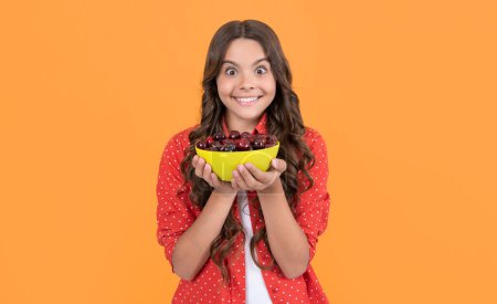 surprised teen girl hold cherry bowl on yellow background.