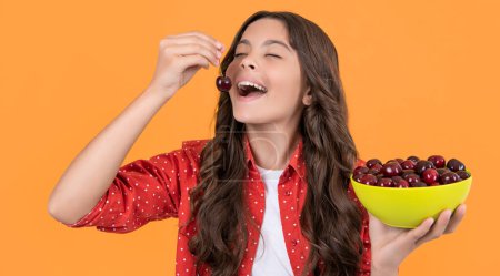 fröhliche Teenager-Mädchen essen Kirschschale auf gelbem Hintergrund.