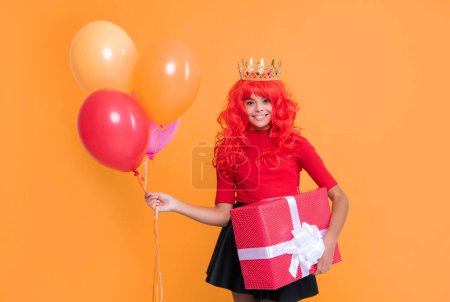smiling girl in crown with present box and party balloon on yellow background.