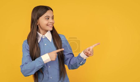 Teenager-Schulmädchen in Uniform machen Werbung. Teenager Mädchen präsentiert Produkt mit Kopierraum. Mädchen zeigt mit dem Finger. Teen Student hat ein glückliches Gesicht. Angebot und Präsentation des Produkts. Exklusives Online-Angebot.