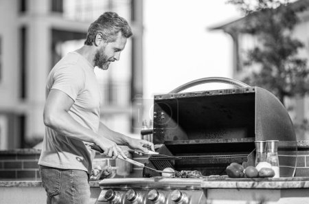 Mann grillt leckeren Grill an einem Sommertag. Mann bereitet Grillgut am Hinterhof-Grill zu. Präzises Grillen. Mann mit heißem Grill bei Grillparty. Schnitzel.