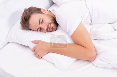 Deep male sleep. Man sleeping at night. Sleepy man lying on bed sleeping at white bedroom. Asleep young man sleeping. Resting peacefully in comfortable bed. Lying with closed eyes. Sick leave.