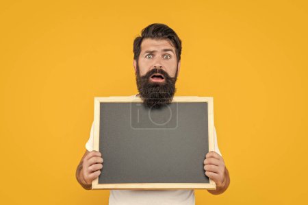 shocked bearded man with advertisement blackboard isolated on yellow. bearded man hold blackboard for advertisement. studio advertisement of man. man at advertisement blackboard with copy space.