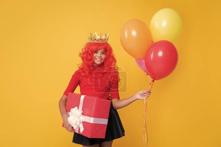 positive girl in crown with present box and party balloon on yellow background.
