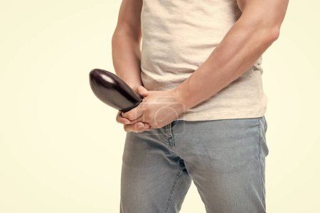 Man crop view holding eggplant at crotch level imitating erect penis isolated on white.