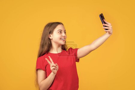 Foto de Niño feliz haciendo selfie en el teléfono inteligente sobre fondo amarillo. - Imagen libre de derechos