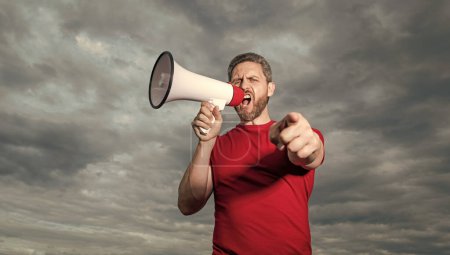 man in red shirt shout in loudspeaker on sky background. point finger.
